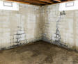 Damp basement with stained concrete walls and floor, exposed ceiling, and two small windows.