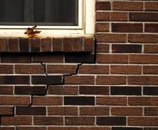 Brick wall with a visible crack beneath a window sill, where leaves have gathered.