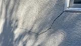 Cracks on a gray stucco exterior wall near a window, with shadows cast on the surface.