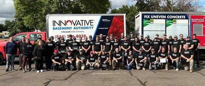 Large group of people in matching black shirts posing in front of Innovative Basement Authority company trucks.