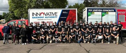 Large group of people in matching black shirts posing in front of Innovative Basement Authority company trucks.