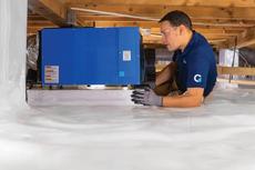 A production member is installing a dehumidifier in the encapsulated crawlspace.