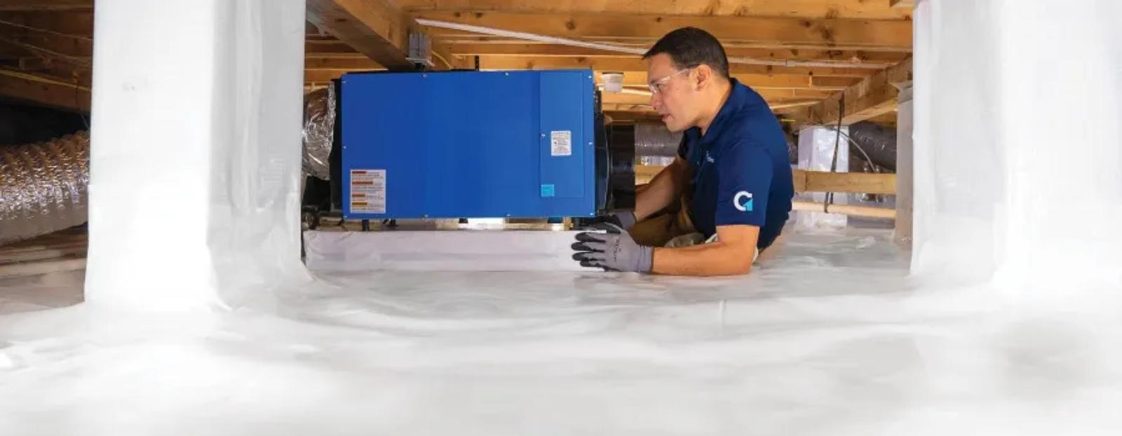 A production member is installing a dehumidifier in the encapsulated crawlspace.