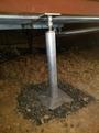 Adjustable metal support post stabilizing a structure above, set on rocky ground.