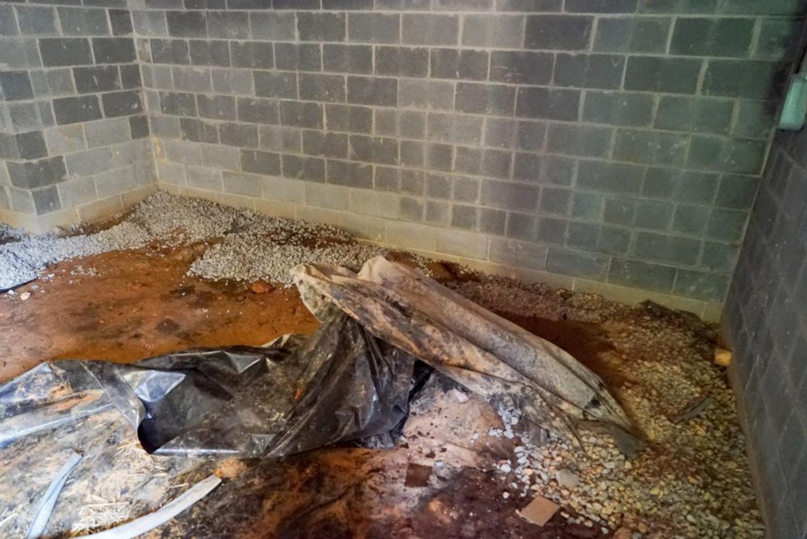 A dimly lit, empty concrete room with debris and a black tarp on the floor.