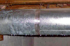 A metal pipe with condensation droplets underneath a wooden beam.