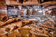 Dirty crawlspace with hanging insulation and open crawlspace vent.