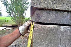 Hands measuring gap in exterior cinderblock wall.