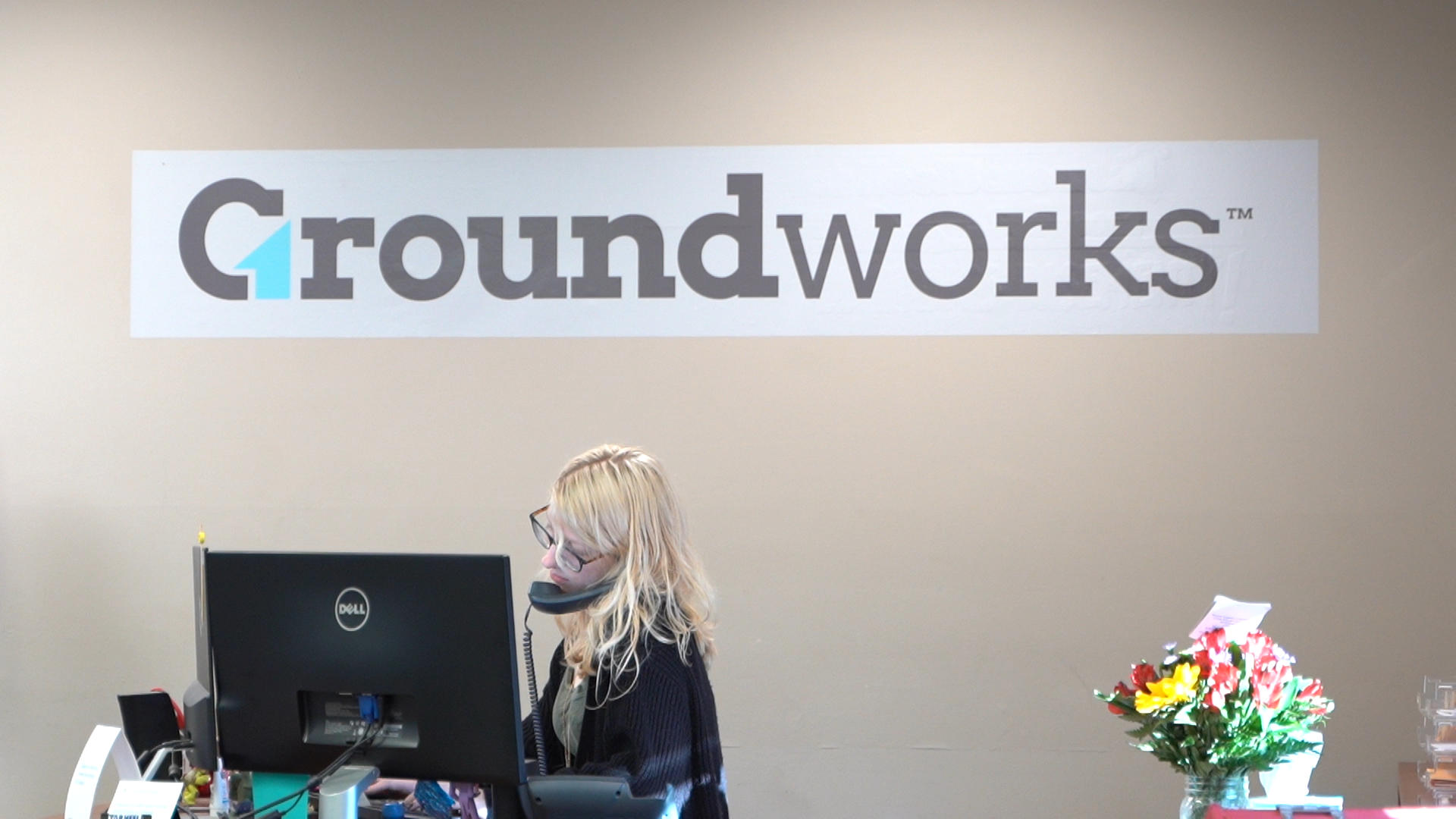 Admin staff on the phone in office with the Groundworks logo in background.