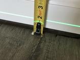 Tape measure against a white baseboard and a green laser level line above wood flooring.