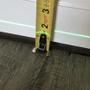 Tape measure against a white baseboard and a green laser level line above wood flooring.