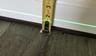 Tape measure against a white baseboard and a green laser level line above wood flooring.