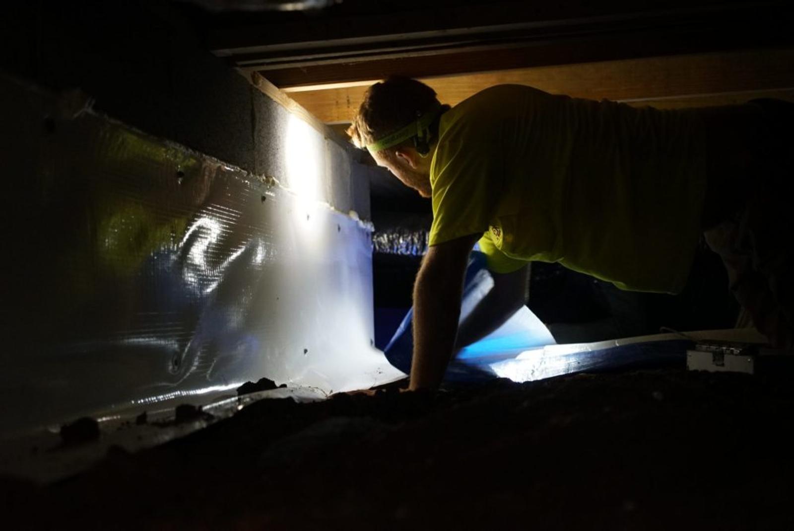 Crew with headlamp installing vapor barrier in crawl space