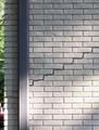 Brick wall with a diagonal crack next to a vertical rain gutter.