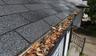Gutter filled with leaves, sticks, and debris along the roof edge of a house.