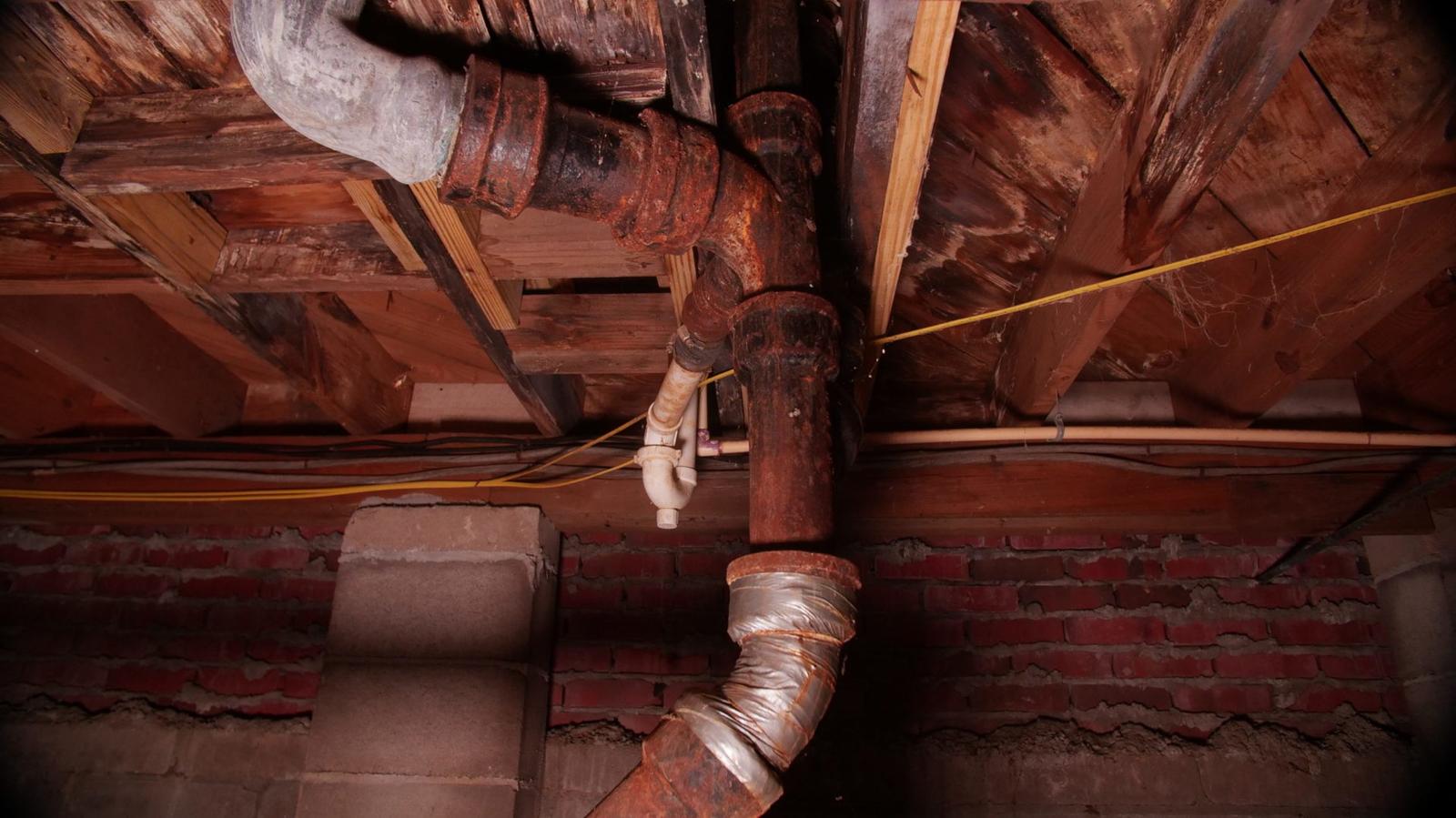 Rusty pipes with rotting wet and moldy crawl space wood