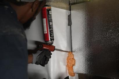 Person using a foam gun to apply insulating foam on a wall.