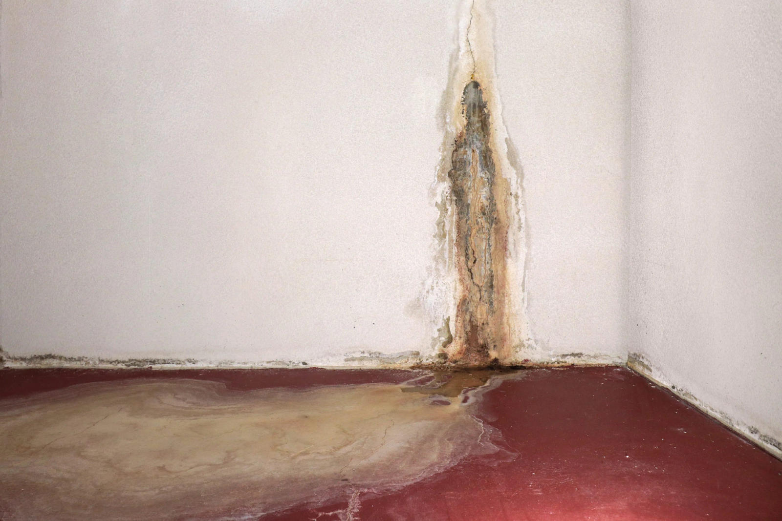 Crack in wall leadinginto floor, with water leaking through