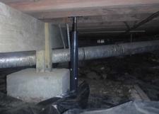 Crawl space with a support beam reinforced by a metal jack and insulated ductwork overhead.