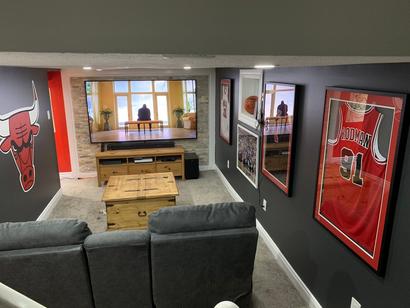 Basement home theater with gray seats, Chicago Bulls decor, and a large TV on a stone accent wall.