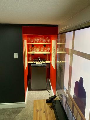 A small wine nook with glass shelves, wine glasses, wine bottles, a mini fridge, and red accent walls.