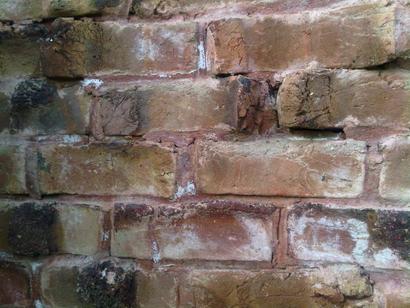 Close-up of an old, weathered brick wall with uneven, cracked bricks and visible mortar lines.