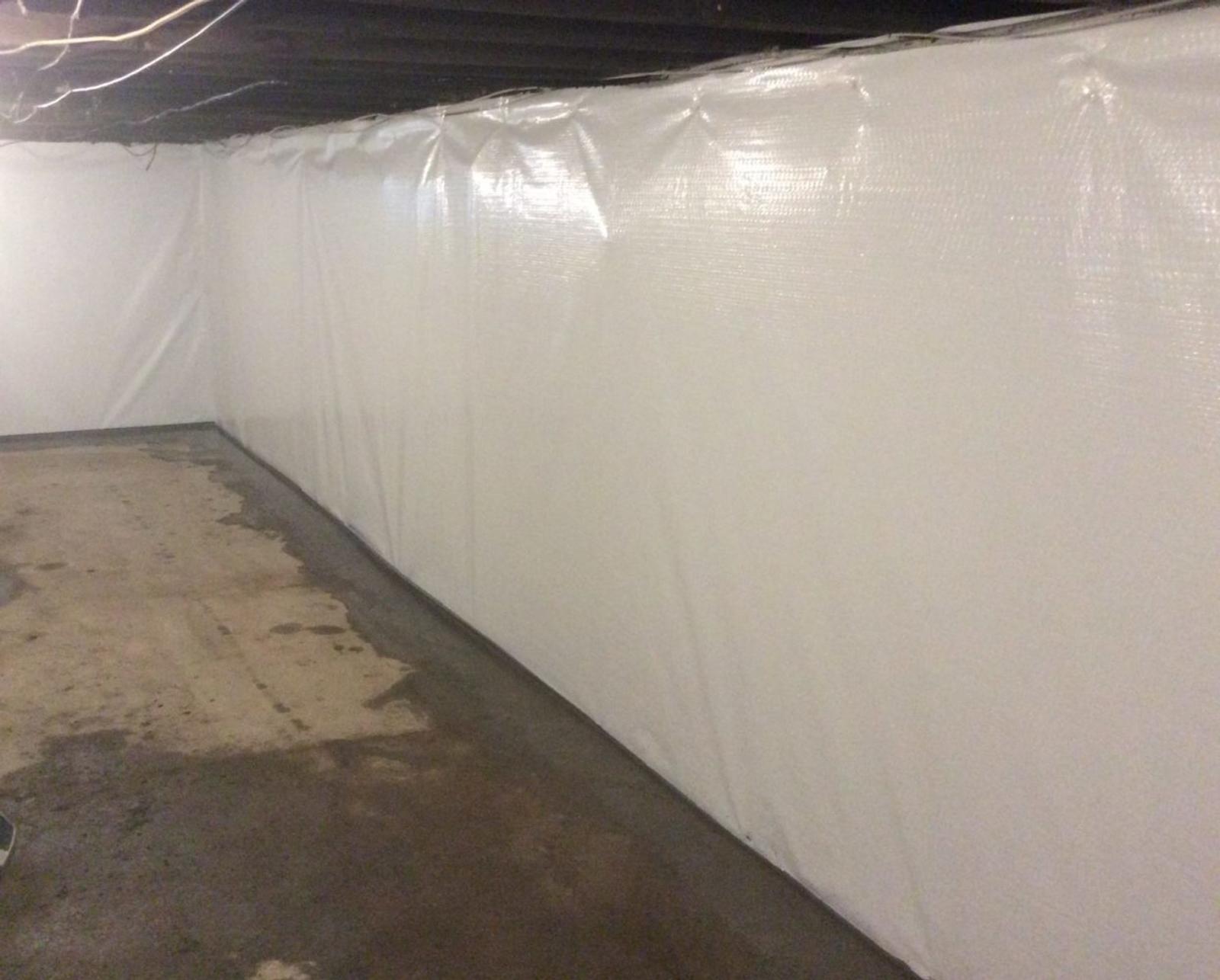 Basement with white plastic-covered walls and a concrete floor, with exposed beams on the ceiling.