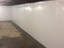 Basement with white plastic-covered walls and a concrete floor, with exposed beams on the ceiling.