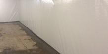 Basement with white plastic-covered walls and a concrete floor, with exposed beams on the ceiling.