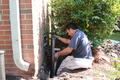 Man working on foundation repair next to a brick wall and bush.