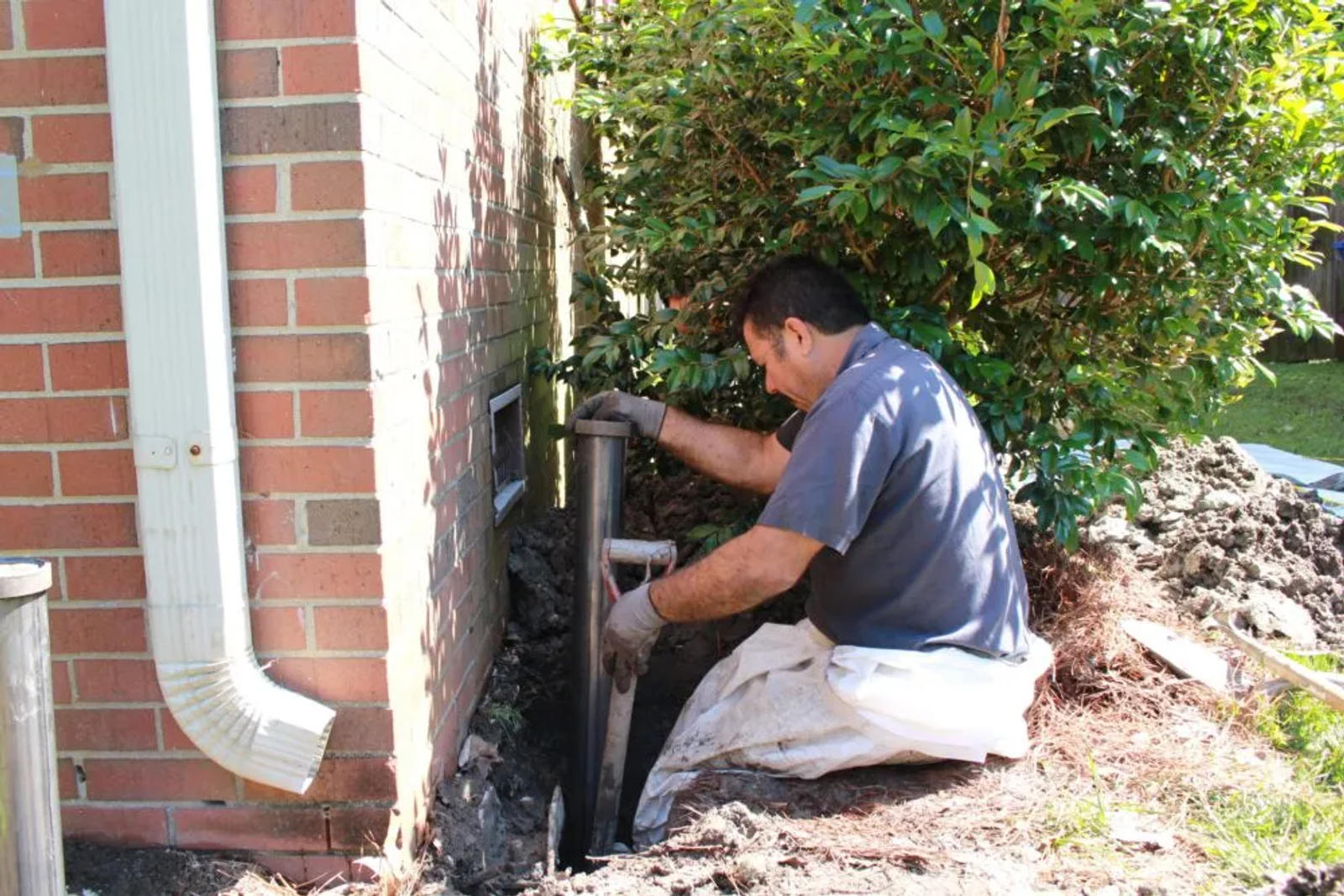 Man working on foundation repair next to a brick wall and bush.