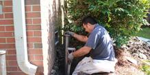Man working on foundation repair next to a brick wall and bush.