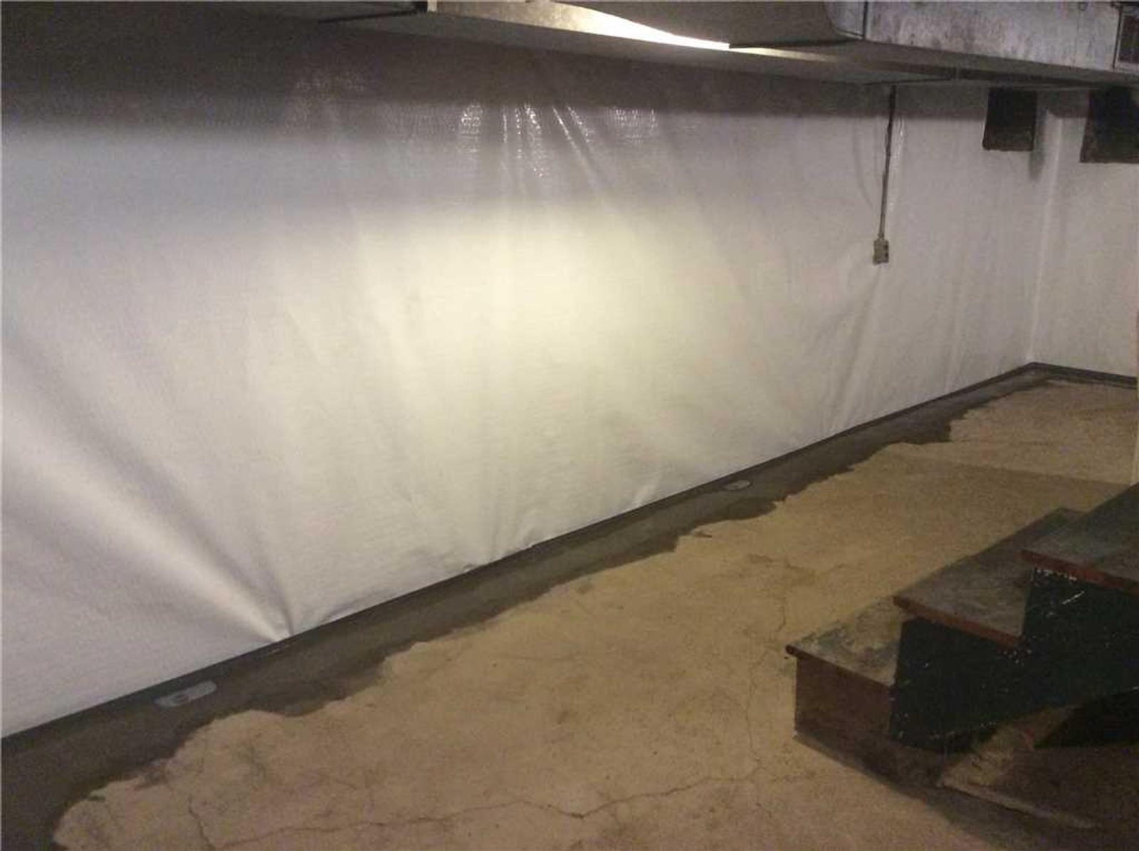 Basement with cracked concrete floor, white wall covering, and partial view of stairs on the right.