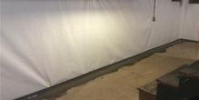 Basement with cracked concrete floor, white wall covering, and partial view of stairs on the right.