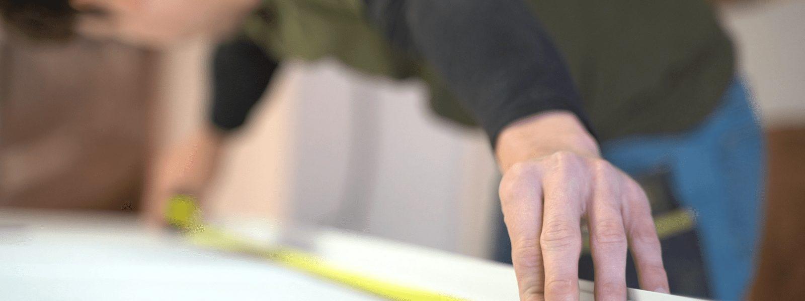Person measuring with a tape measure on a surface, focus on their hand.