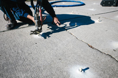 Person using a tool to fill holes in concrete pavement under bright sunlight.