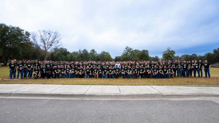 A large group of people wearing matching shirts pose outdoors on a cloudy day.