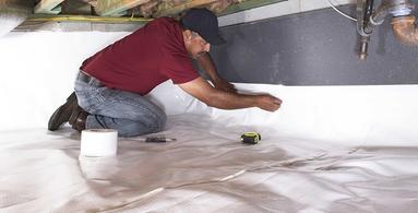 Crew installing a vapor barrier in crawlspace.