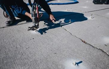 Crew injecting poly into uneven walkway for lifting and leveling.
