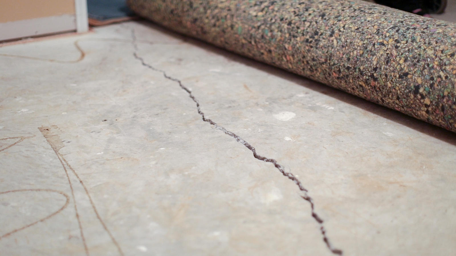 Concrete floor with a long crack visible, and a rolled-up carpet pad nearby.