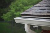 Close-up of a rain-soaked roof and gutter with a blurred green background.