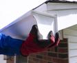 Person wearing red and black gloves installing a white gutter on a house.