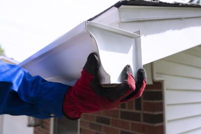 Person wearing red and black gloves installing a white gutter on a house.