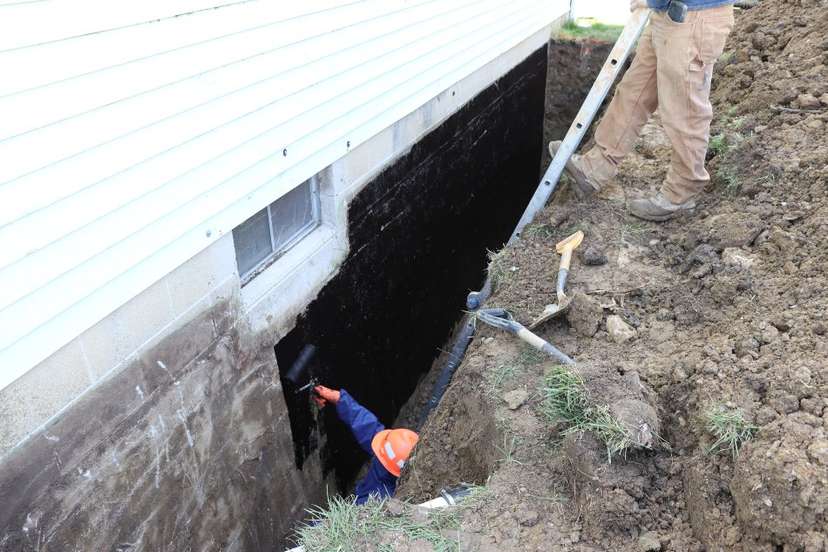 construction workers damp-proofing home exterior