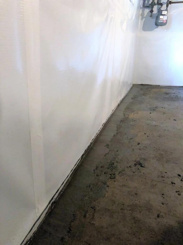 Basement with a sealed and painted wall, concrete floor, and exposed utility pipes in the corner.