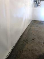 Basement with a sealed and painted wall, concrete floor, and exposed utility pipes in the corner.