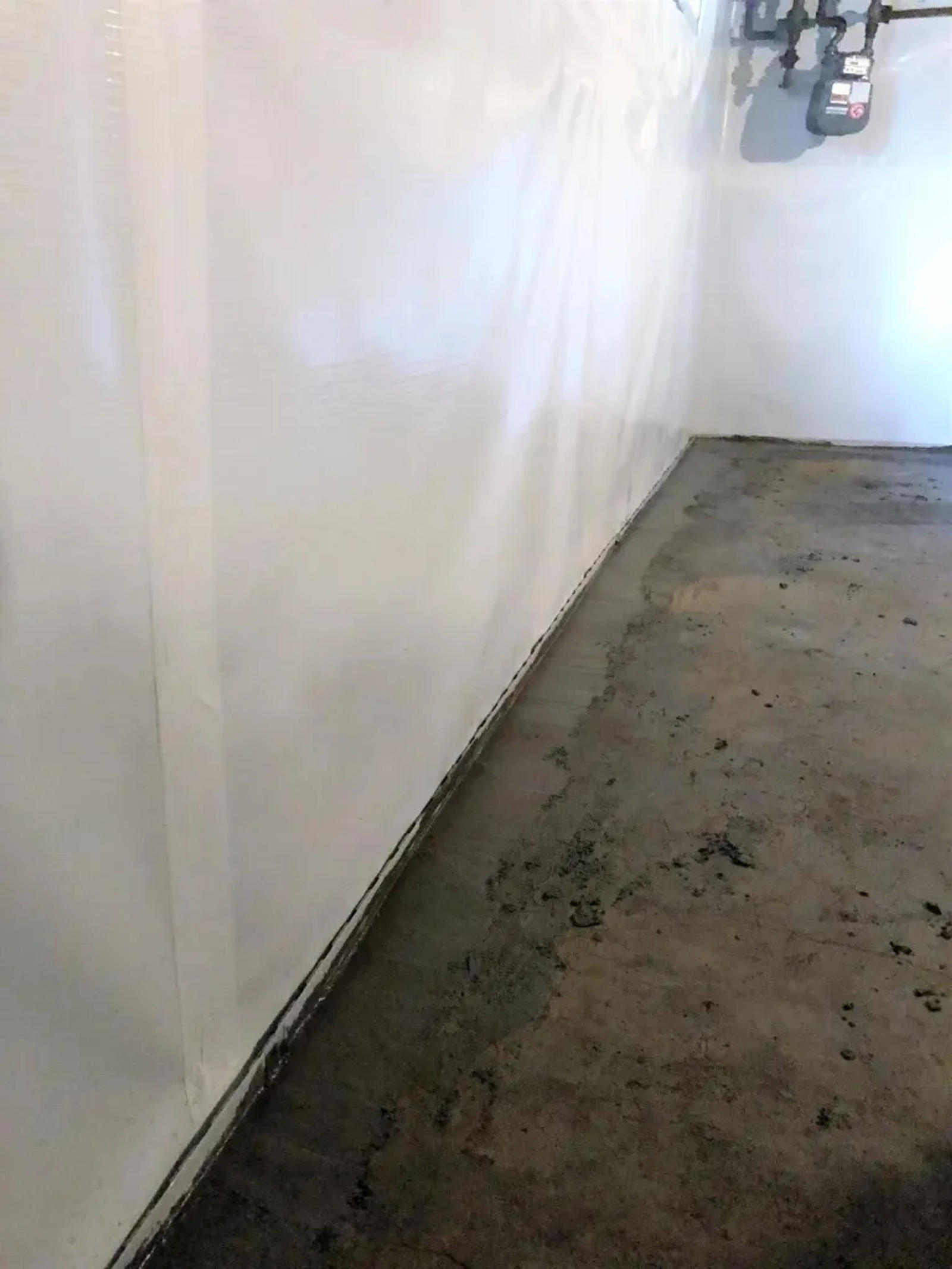 Basement with a sealed and painted wall, concrete floor, and exposed utility pipes in the corner.