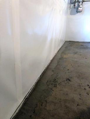 Basement with a sealed and painted wall, concrete floor, and exposed utility pipes in the corner.