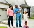 A family is smiling and standing outside of their home.