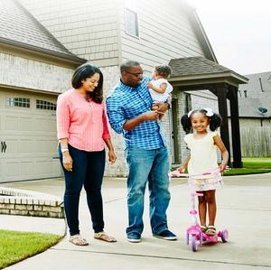 A family is smiling and standing outside of their home.